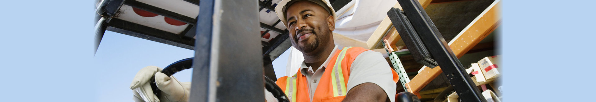 Low angle view of a happy male industrial worker driving forklift at workplace